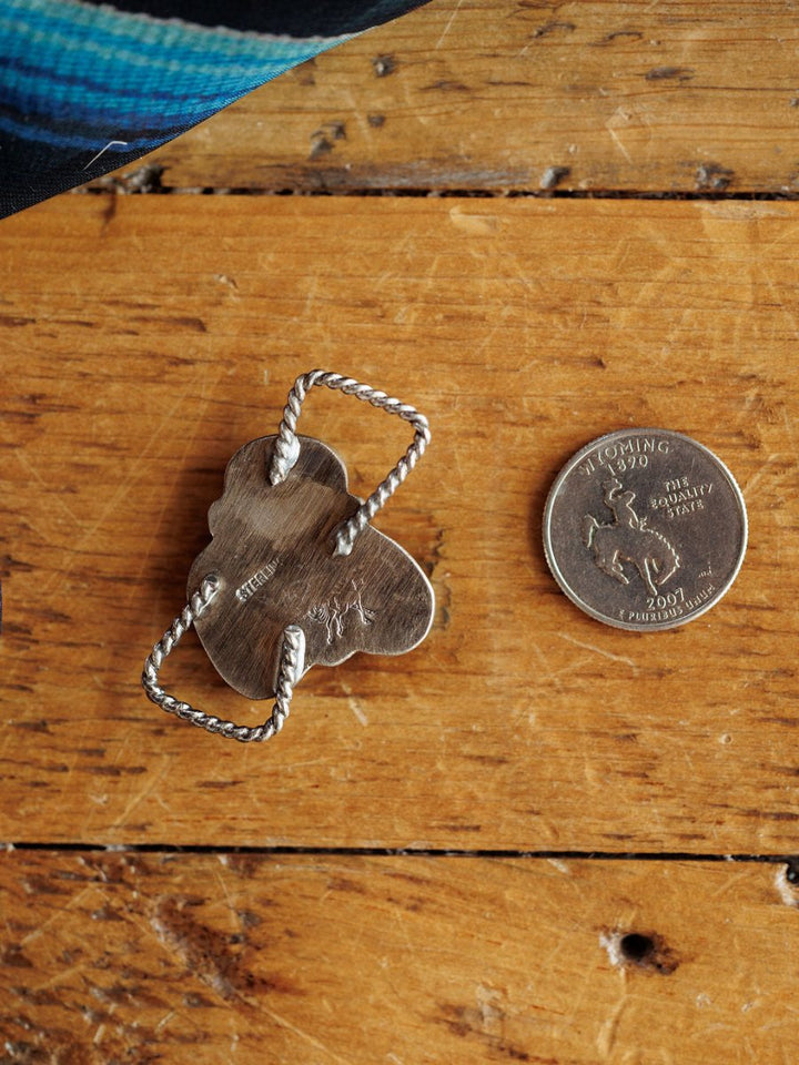 A silver ring with a twisted band and "STERLING" mark lies beside a Wyoming quarter on wood. At the top left is a blue patterned fabric, perfect for pairing with the Etowah Scarf Pendant by Savannah Sevens western life{&}style.