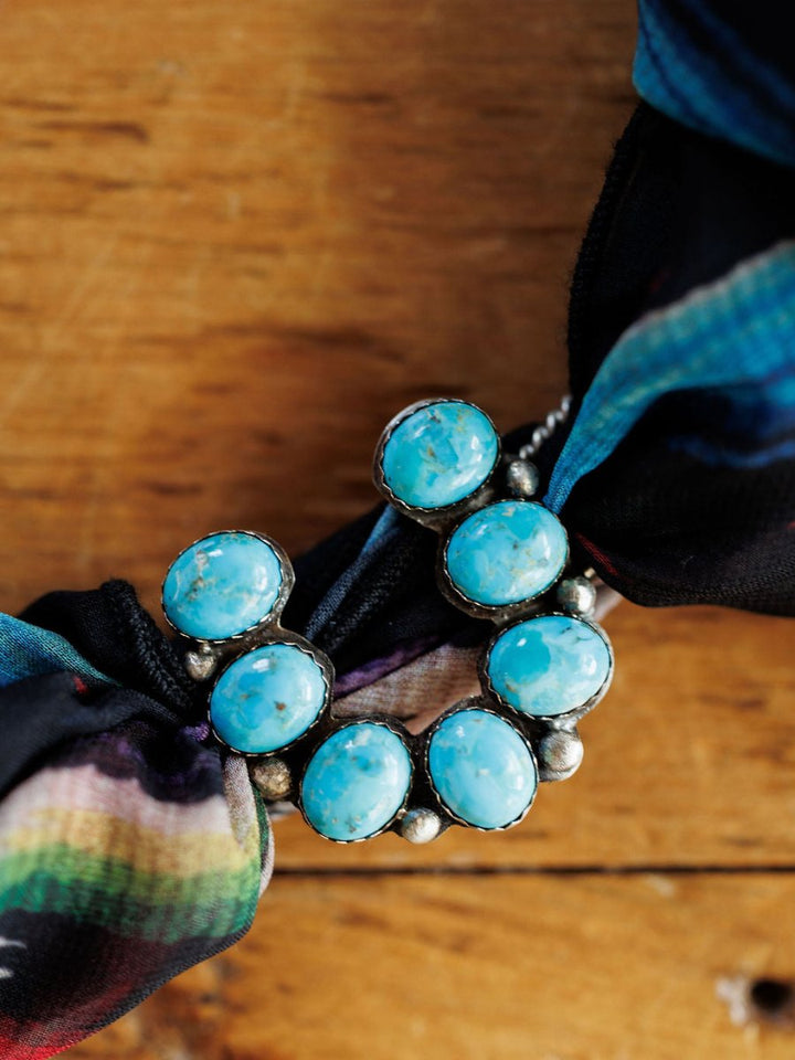 A close-up of the Etowah Scarf Pendant by Savannah Sevens western life{&}style, displayed on a wooden surface and partially draped with a colorful patterned fabric.