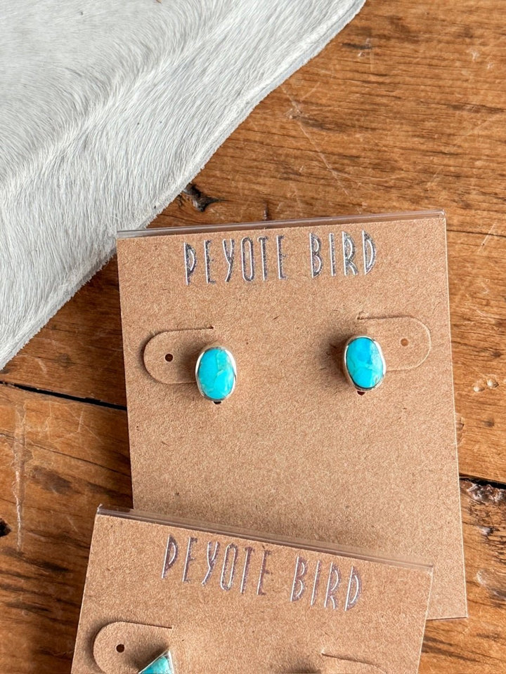 A pair of Falcon Earrings by Savannah Sevens western life{&}style displayed on a brown card, set on a wooden surface next to light gray textured fabric.