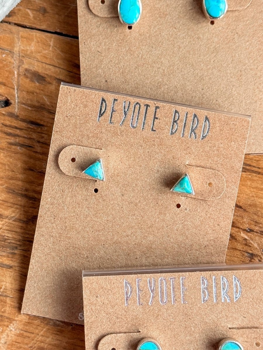 Brown cards labeled Savannah Sevens western life{&}style display Falcon Earrings, including small triangle-shaped turquoise studs set in sterling silver, all arranged on a rustic wooden surface.