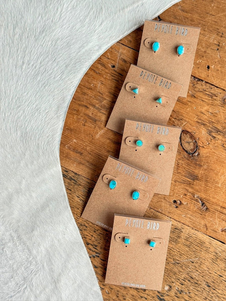 Five pairs of Falcon Earrings by Savannah Sevens western life{&}style are arranged diagonally on brown Peyote Bird cards atop a wooden surface, beside light grey furry fabric.