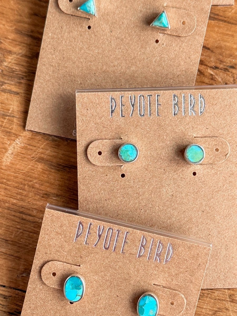 Three pairs of Falcon Earrings by Savannah Sevens western life{&}style—one triangle pair and two turquoise stud pairs in sterling silver—are displayed on brown cards labeled PEYOTE BIRD on a wooden surface.