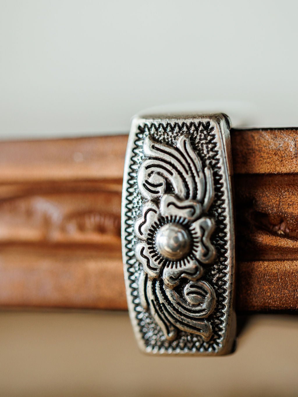 A close-up of an ornate silver clip with floral and geometric patterns attached to the Fayetteville Belt by Savannah Sevens western life{&}style, crafted in a hand-tooled leather design.