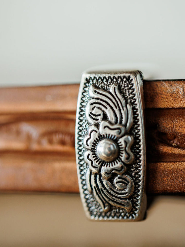A close-up of an ornate silver clip with floral and geometric patterns attached to the Fayetteville Belt by Savannah Sevens western life{&}style, crafted in a hand-tooled leather design.