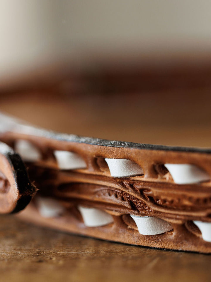 A close-up of the Fayetteville Belt by Savannah Sevens western life{&}style, showcasing intricate hand tooling and white decorative stitching throughout the leather design.