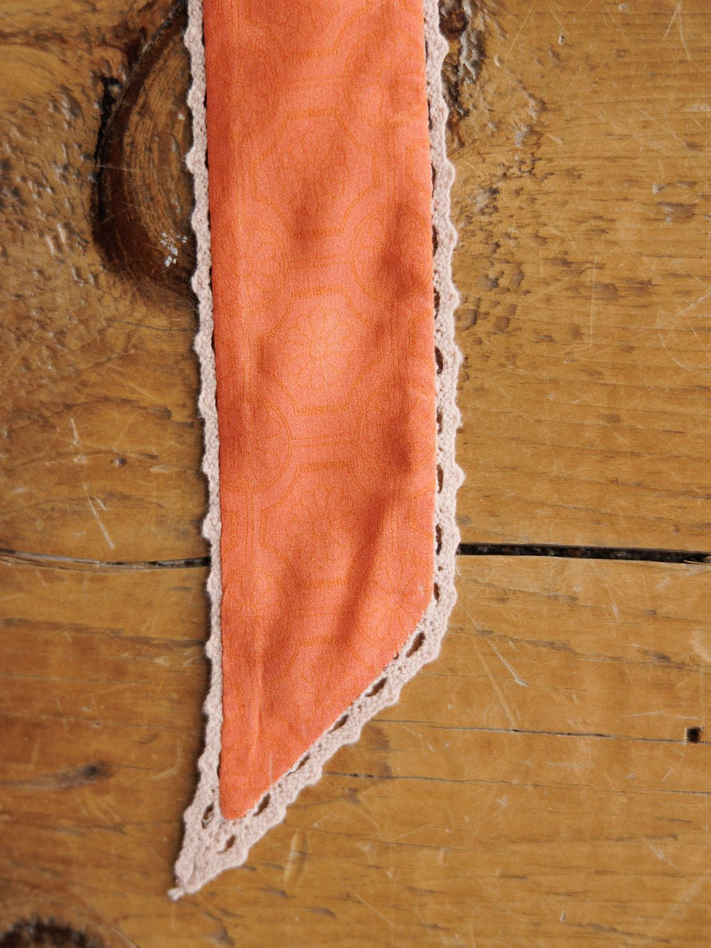 A close-up of the Frankie Twilly by Savannah Sevens western life{&}style, featuring pointed orange fabric with a subtle pattern and crochet trim, displayed on a rustic wooden surface.