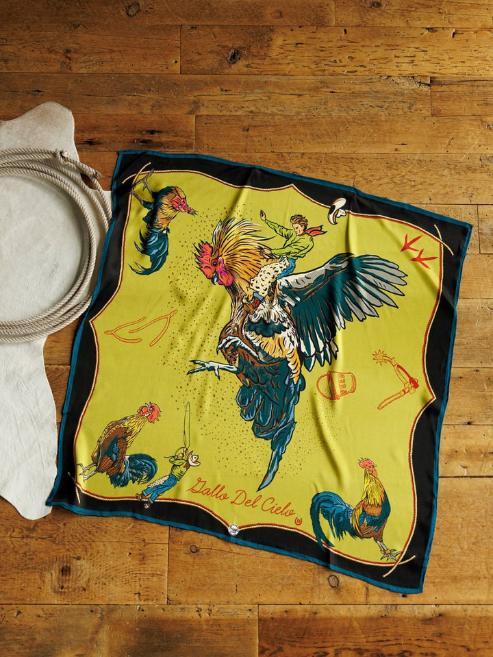 The Gallo Del Cielo Wild Rag by Savannah Sevens western life{&}style is a colorful silk scarf featuring rooster illustrations, western-themed designs, and "Gallo Del Cielo" text at the bottom.