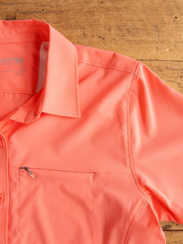 The top left of the Galva Ariat Coral Performance Shirt by Savannah Sevens western life{&}style, featuring short sleeves, a front pocket, zipper detail, and moisture-wicking fabric, is shown on a wooden surface.