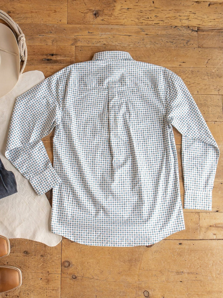 The Georgetown Wrangler Men's Southwest Button Up from Savannah Sevens western life{&}style features a small blue and tan check pattern. It is laid flat, back facing up, on a wooden floor beside a hat and tan fabric.