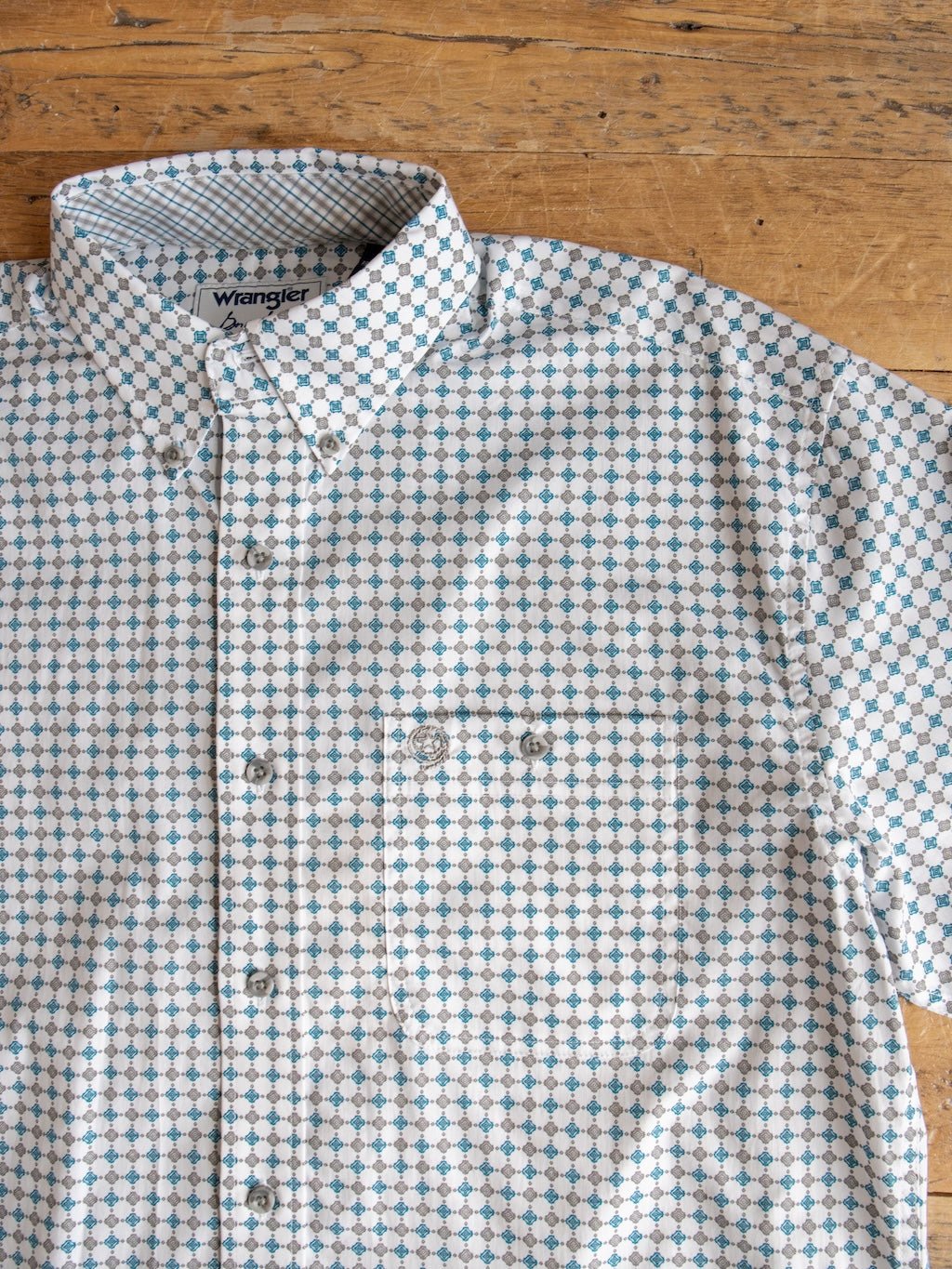 A Savannah Sevens western life{&}style Georgetown Wrangler Men's Southwest Button Up shirt featuring a blue and gray geometric dot pattern is laid flat on a wooden surface.