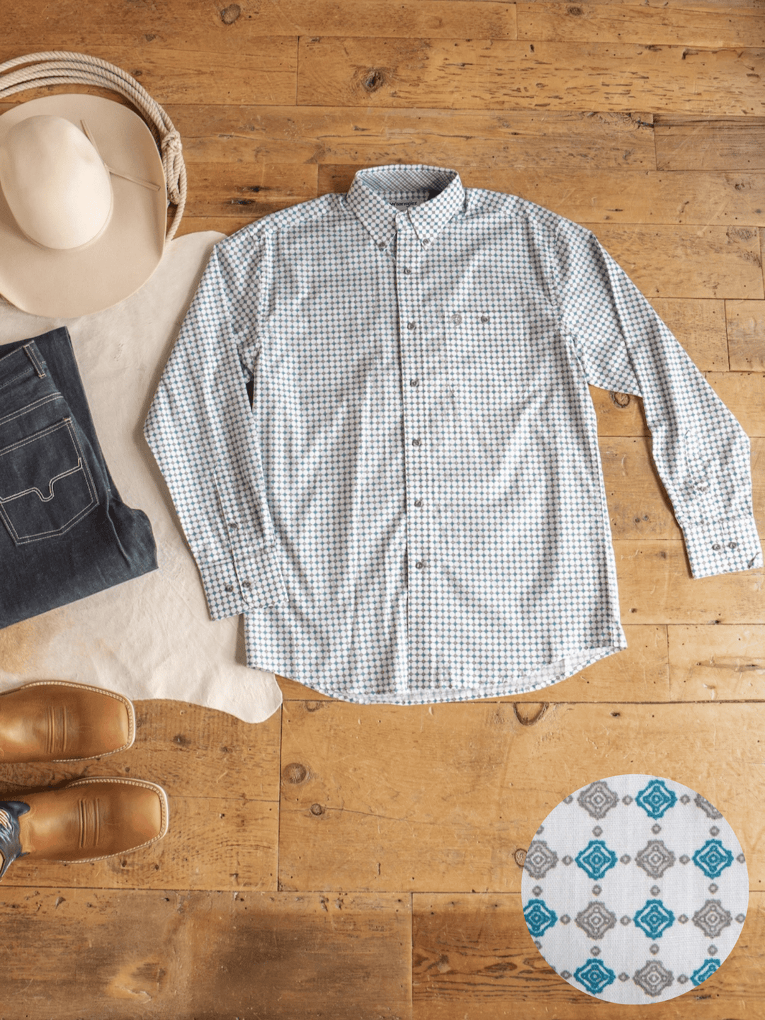 A Georgetown Wrangler Men's Southwest Button Up from Savannah Sevens western life{&}style is laid out on a wooden floor with jeans, cowboy hat, boots, and a close-up of the shirt’s blue and gray geometric pattern.