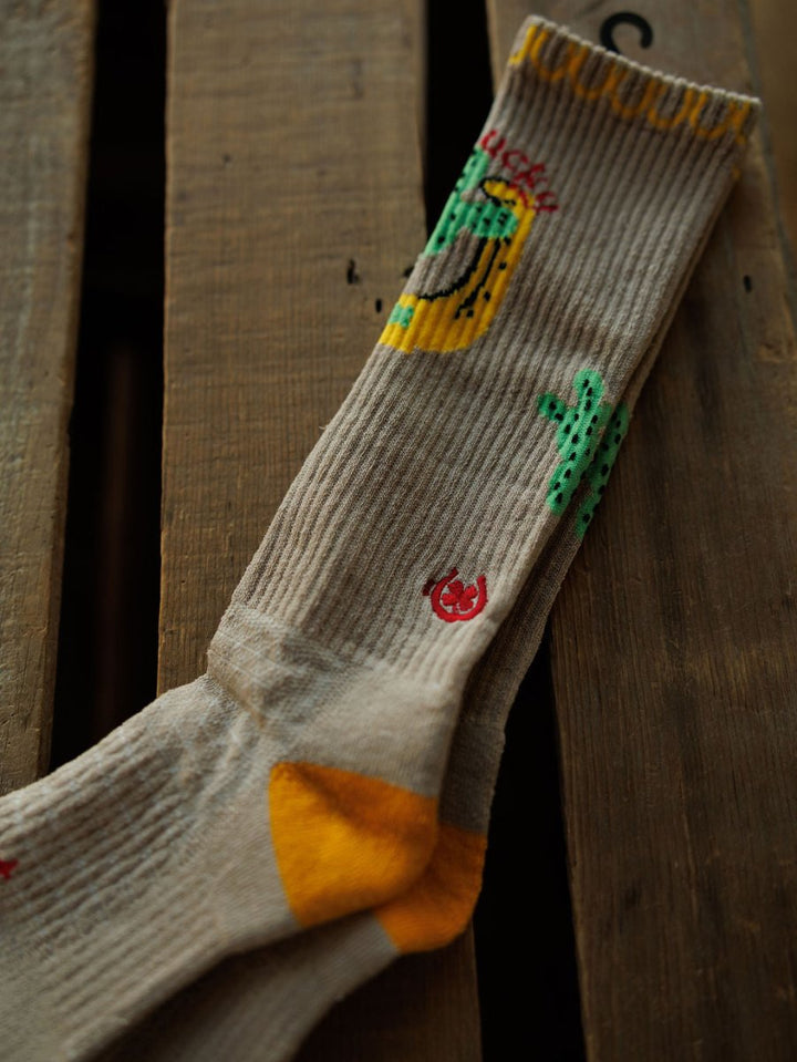 The Get Lucky Crew Socks {Tan} by Savannah Sevens western life{&}style feature cactus and sombrero motifs, a yellow heel, and are made from an odor-fighting hemp blend for lightweight, breathable comfort.