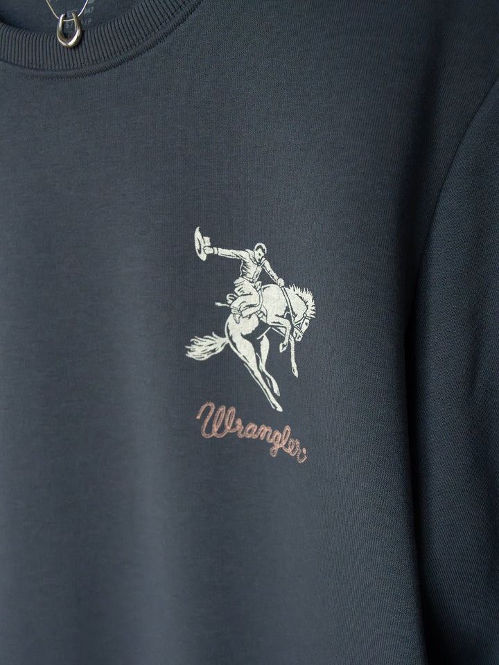 Close-up of the Gillette Slate Western Graphic Pullover by Savannah Sevens western life{&}style features a dark western design with a saddle bronc logo depicting a cowboy riding a bucking horse above the word "Wrangler" in script.