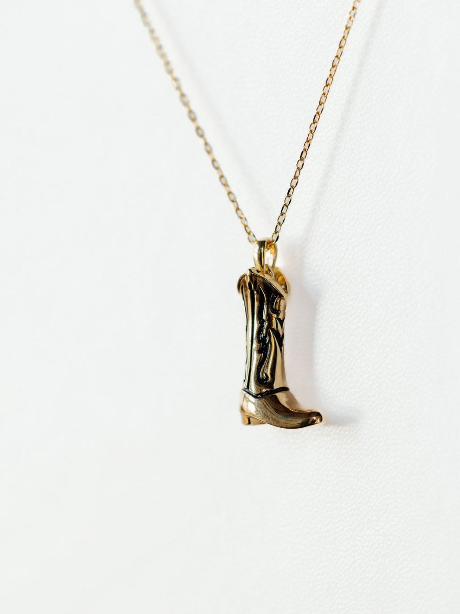 The Gold Cowgirl Boot Necklace by Savannah Sevens western life{&}style features a 14K yellow gold plated cowboy boot pendant, shown on a plain white background—a western jewelry piece that adds stylish flair to any outfit.