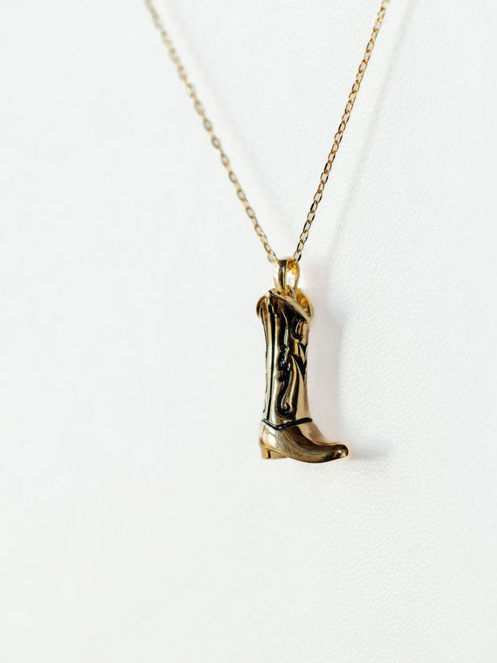 The Gold Cowgirl Boot Necklace by Savannah Sevens western life{&}style features a 14K yellow gold plated cowboy boot pendant, shown on a plain white background—a western jewelry piece that adds stylish flair to any outfit.