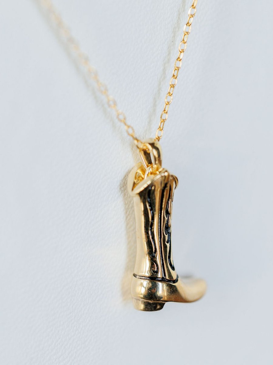 The Gold Cowgirl Boot Necklace by Savannah Sevens western life{&}style features a 14K yellow gold plated cowboy boot design, shown on a white background—a perfect western jewelry accent for your outfit.