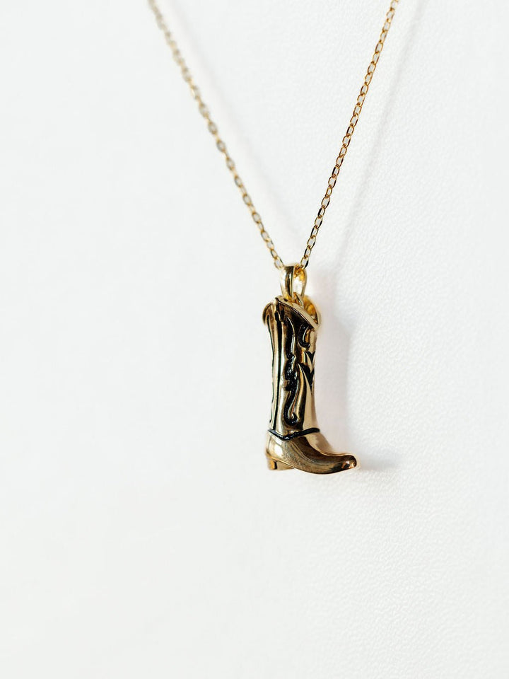 The Gold Cowgirl Boot Necklace by Savannah Sevens western life{&}style features a 14K yellow gold plated cowboy boot pendant, shown on a plain white background—a western jewelry piece that adds stylish flair to any outfit.