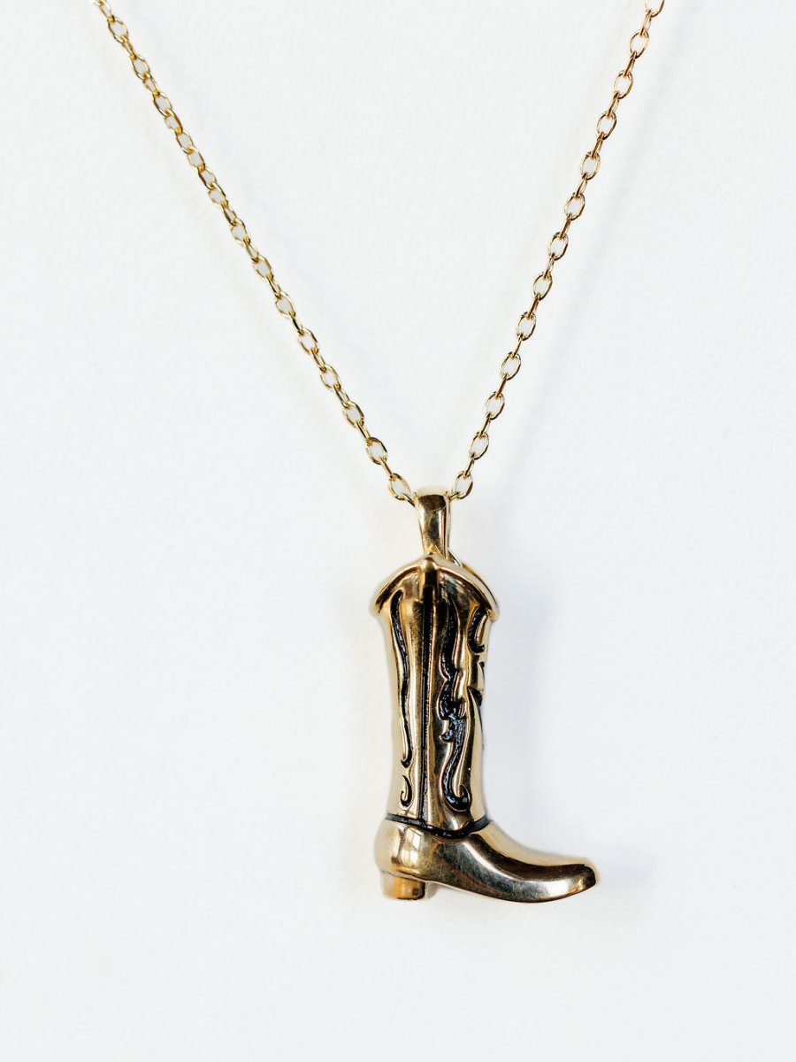 The Gold Cowgirl Boot Necklace by Savannah Sevens western life{&}style features engraved 14K yellow gold plating and a cowgirl boot charm, making it a stylish western accessory for any outfit. Displayed on a plain white background.