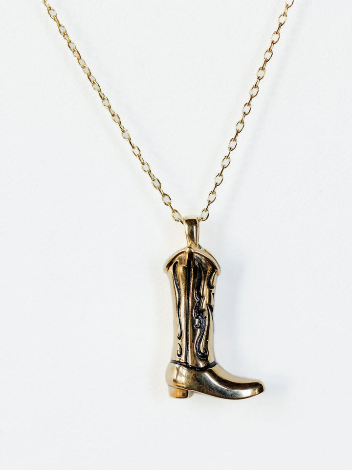 The Gold Cowgirl Boot Necklace by Savannah Sevens western life{&}style features engraved 14K yellow gold plating and a cowgirl boot charm, making it a stylish western accessory for any outfit. Displayed on a plain white background.