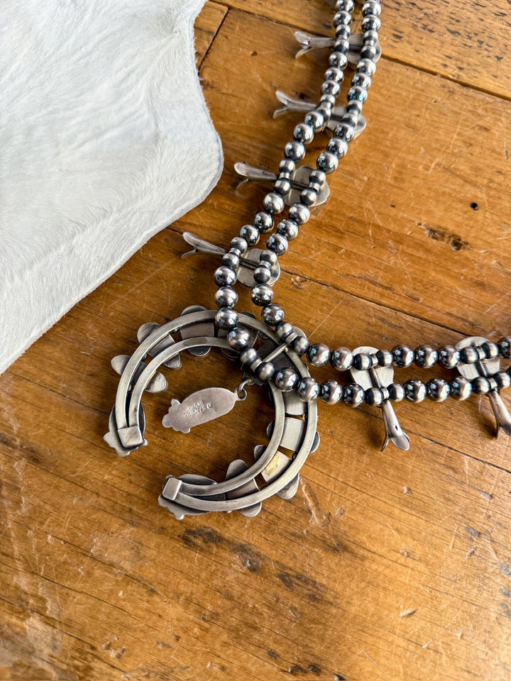 The Golden Hills Necklace & Earrings Set by Savannah Sevens western life&style features round Navajo pearls and a horseshoe-shaped pendant, shown on wood beside white cowhide.