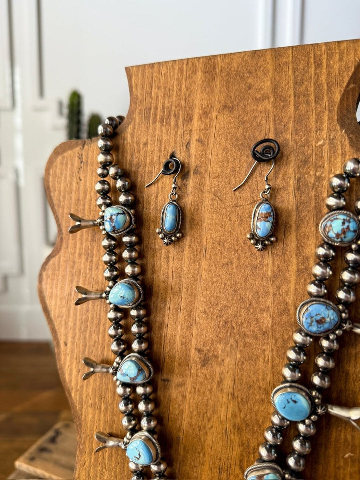The Golden Hills Necklace & Earrings Set by Savannah Sevens western life&style is displayed on a wooden jewelry stand, with a softly blurred white wall and plant in the background.