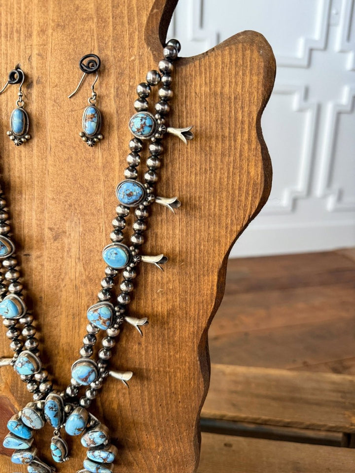 The Golden Hills Necklace & Earrings Set by Savannah Sevens western life&style is displayed on a wooden jewelry stand, with a white decorative wall in the background.