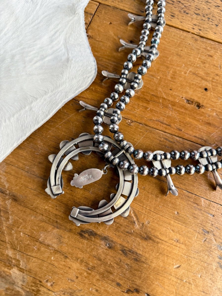 The Golden Hills Necklace & Earrings Set by Savannah Sevens western life&style features round Navajo pearls and a horseshoe-shaped pendant, shown on wood beside white cowhide.