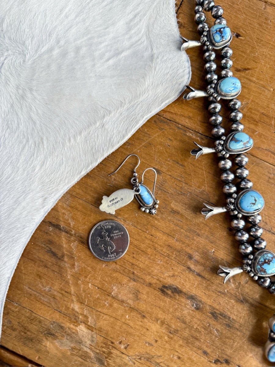 The Golden Hills Necklace & Earrings Set by Savannah Sevens western life&style, featuring elegant sterling silver and vibrant turquoise, rests with a U.S. quarter on wood beside light gray textured fabric.