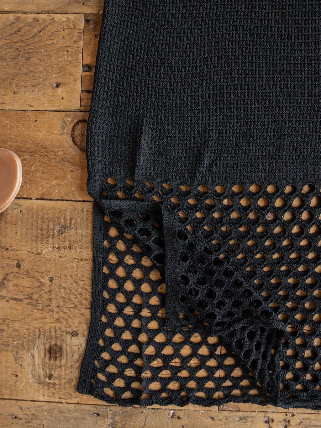 A black crochet fabric from the Granada Black Crochet Dress by Savannah Sevens western life{&}style is displayed on a rustic wooden surface, with one corner folded over to reveal its intricate mesh-edge detail—evoking the sheer accents of its v-neck design.