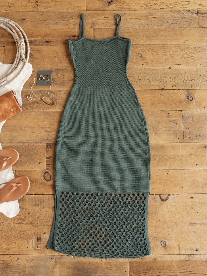 The Granada Blue Sage Crochet Dress by Savannah Sevens western life{&}style is a sleeveless, full-length crochet dress in green with petite adjustable straps and a sheer open-knit pattern at the lower hem, displayed flat on a wooden floor alongside sandals, jewelry, and a bag.