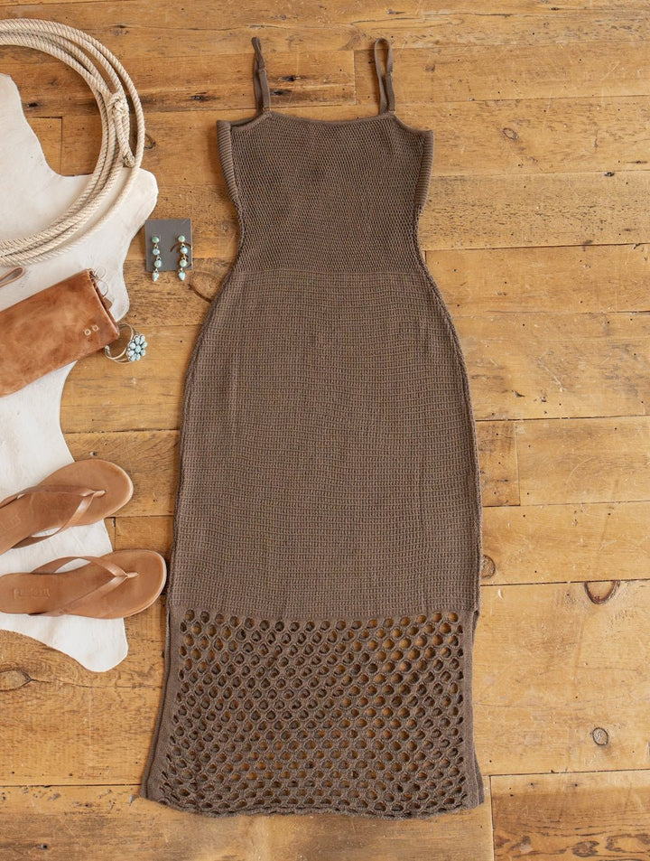 The Savannah Sevens western life{&}style Granada Chocolate Crochet Dress, a sleeveless brown crochet piece with a mesh pattern at the hem, is laid flat on a wooden floor and surrounded by tan sandals, a suede bag, turquoise earrings, and a coiled rope.