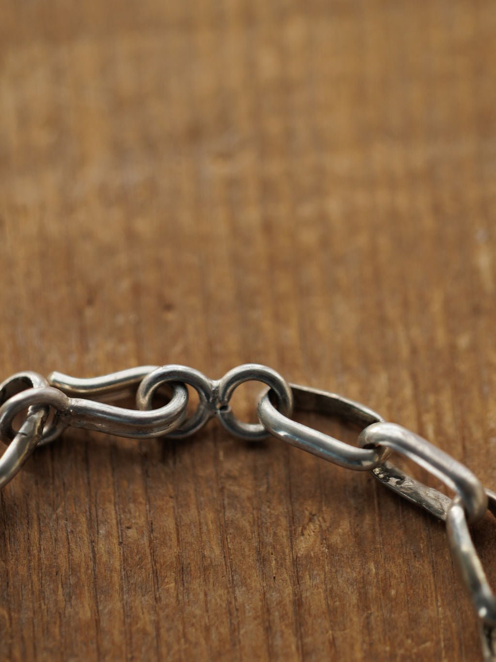 A close-up of the Granada Necklace by Savannah Sevens western life{&}style, featuring a sterling silver chain with a hook clasp on wood. The slightly tarnished links and clasp highlight the necklace's unique texture and character.