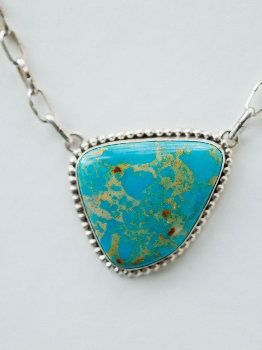 A close-up of the Granada Necklace by Savannah Sevens western life{&}style, showcasing a large triangular Kingman turquoise stone with brown and green flecks, bordered by beaded sterling silver, on a white background.