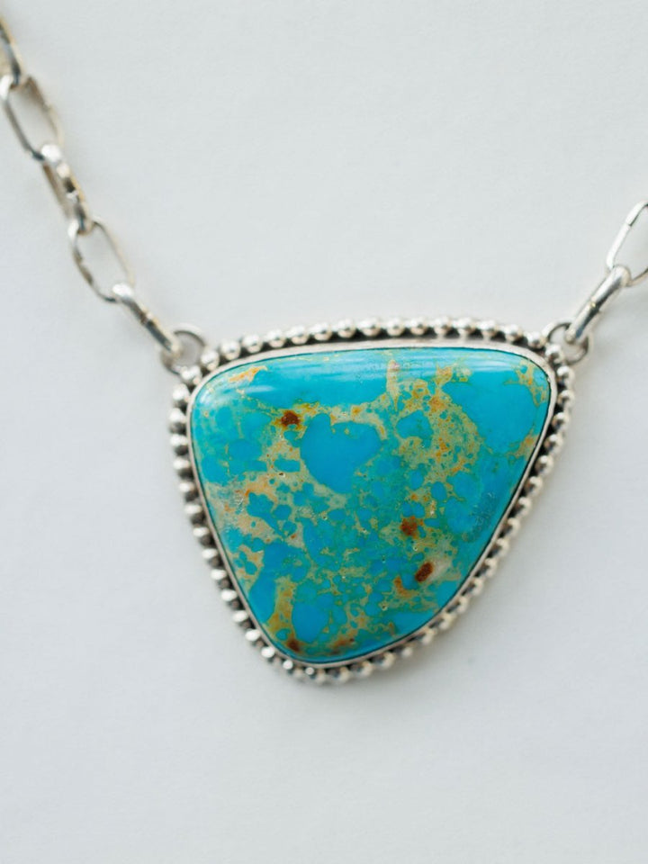 A close-up of the Granada Necklace by Savannah Sevens western life{&}style, showcasing a large triangular Kingman turquoise stone with brown and green flecks, bordered by beaded sterling silver, on a white background.