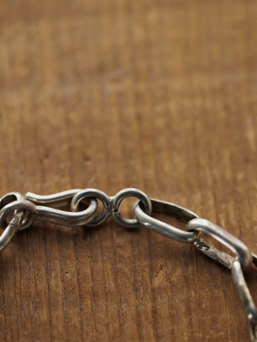 A close-up of the Granada Necklace by Savannah Sevens western life{&}style, featuring a sterling silver chain with a hook clasp on wood. The slightly tarnished links and clasp highlight the necklace's unique texture and character.