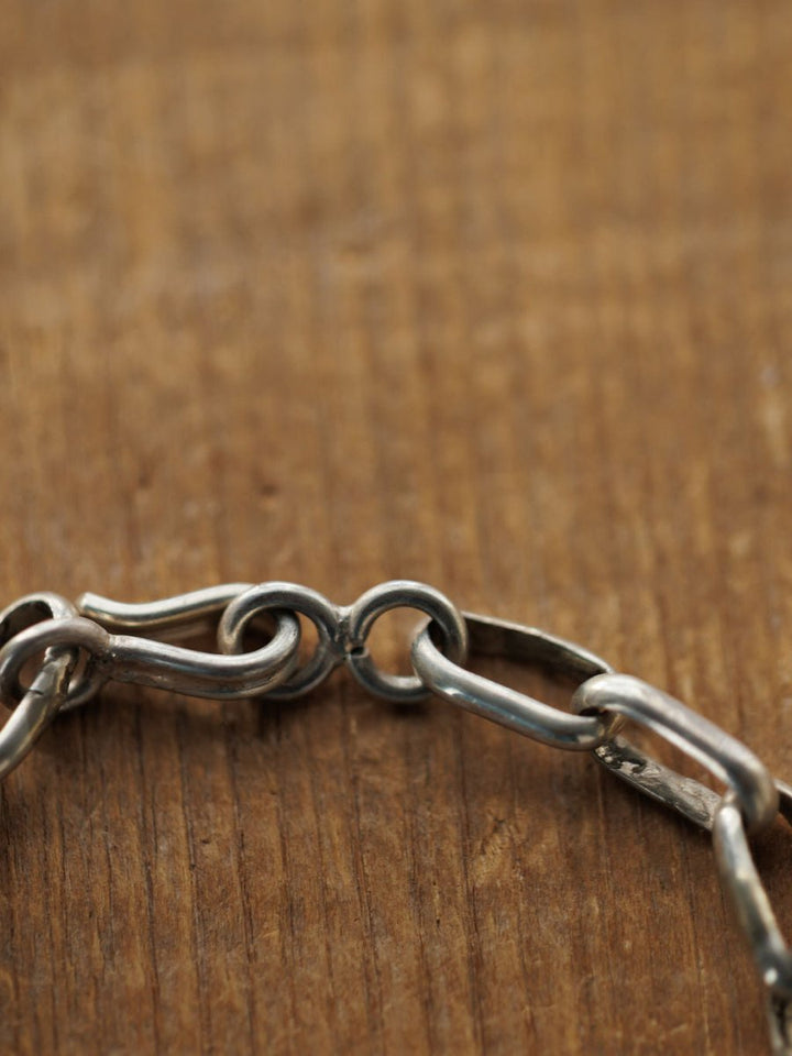 A close-up of the Granada Necklace by Savannah Sevens western life{&}style, featuring a sterling silver chain with a hook clasp on wood. The slightly tarnished links and clasp highlight the necklace's unique texture and character.
