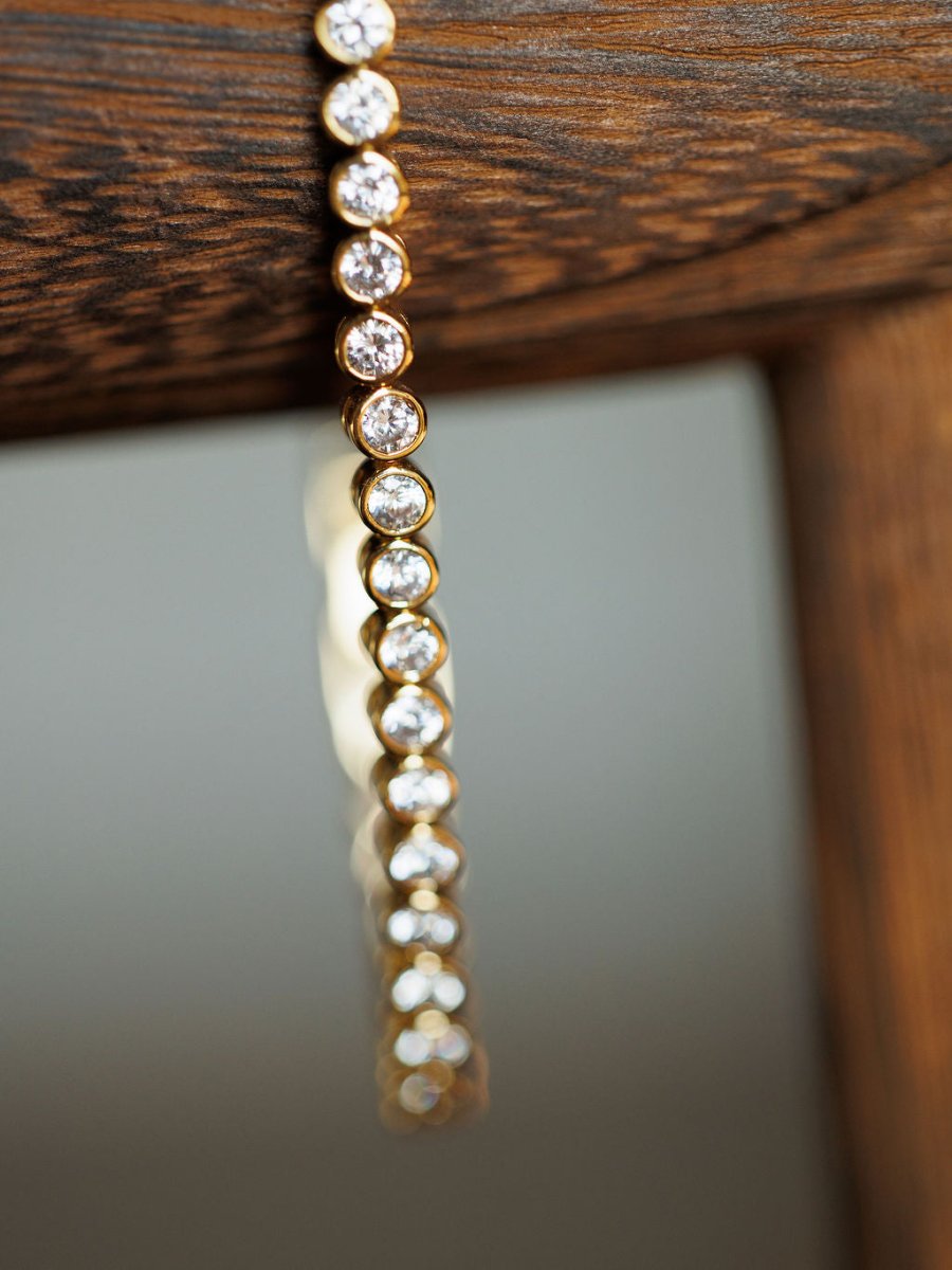 A close-up of the Granby Bracelet by Savannah Sevens western life{&}style, an 18K gold plated piece adorned with round diamonds, elegantly draped over wood with a softly blurred background.