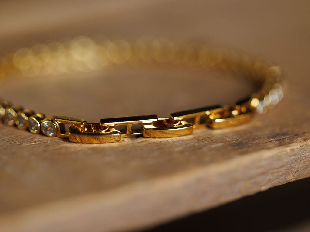 Close-up of the Granby Bracelet by Savannah Sevens western life{&}style, featuring rectangular 18K gold plated links and round clear gemstones, resting on wood. The softly focused shot highlights the shine of this hypoallergenic piece.