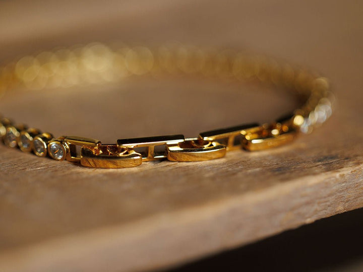 Close-up of the Granby Bracelet by Savannah Sevens western life{&}style, featuring rectangular 18K gold plated links and round clear gemstones, resting on wood. The softly focused shot highlights the shine of this hypoallergenic piece.