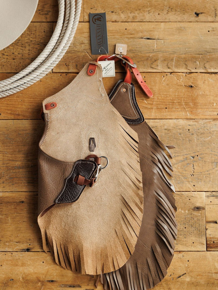The Granger Chinks {Youth} by Savannah Sevens western life{&}style, featuring fringe and a belt buckle, rest on a wooden surface beside a coiled rope.