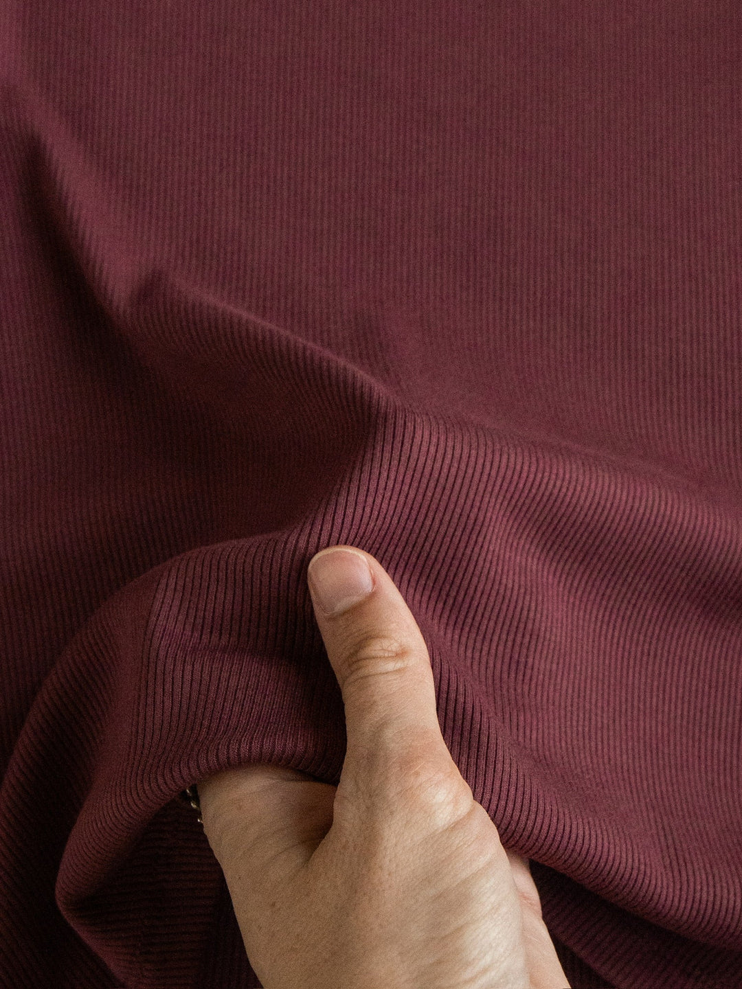 A hand gently pinching and lifting the Hadley Rosewood Ribbed Basic Tee by Savannah Sevens western life{&}style, highlighting the textured ribbed fabric and stretch of this fitted top.