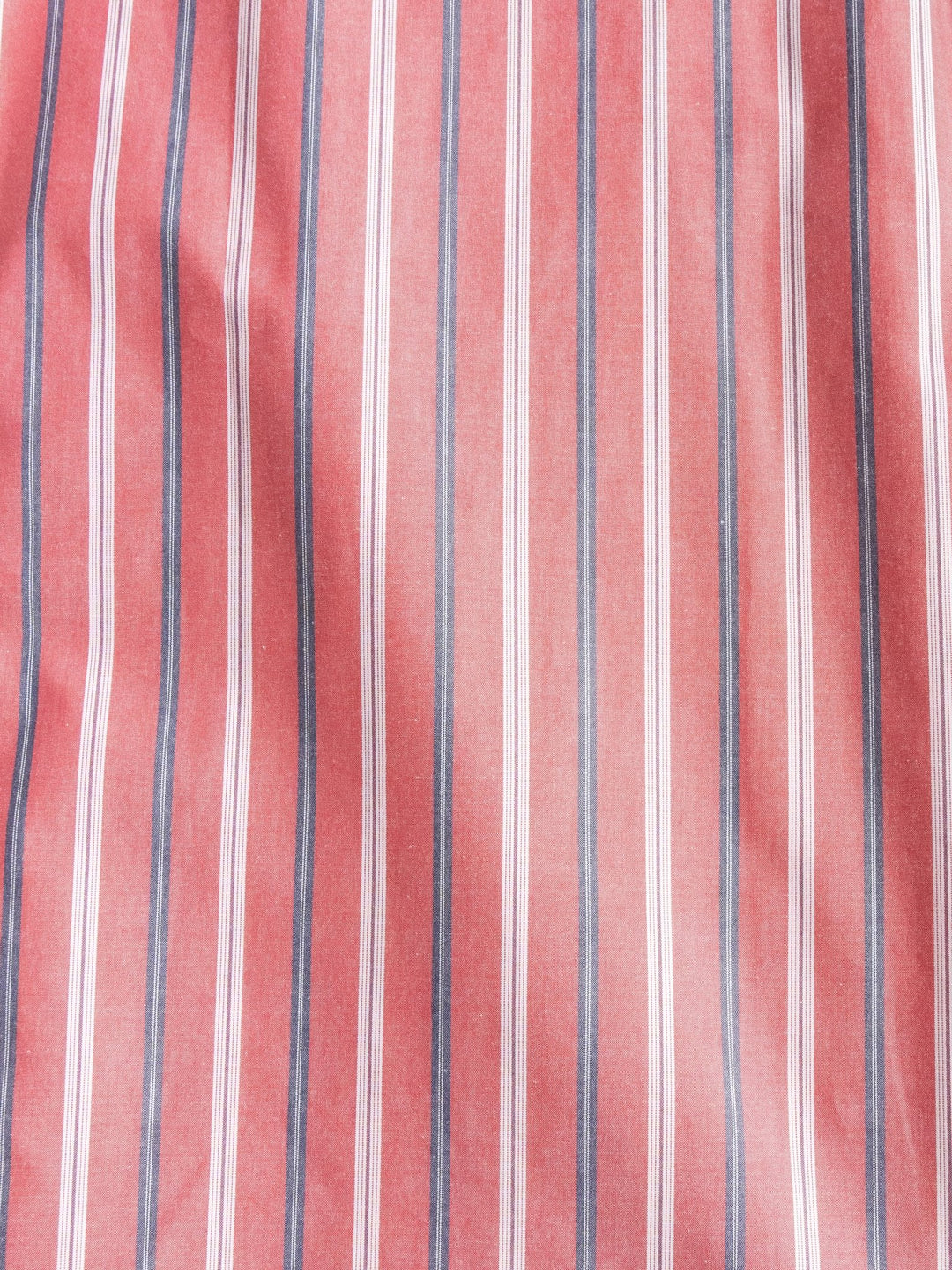 The Hallsburg Ariat Men's Retro Striped Button Up by Savannah Sevens western life{&}style features red fabric with vertical white and dark blue stripes, resembling classic men's shirts. Slight wrinkles create soft folds and shadows on the surface.