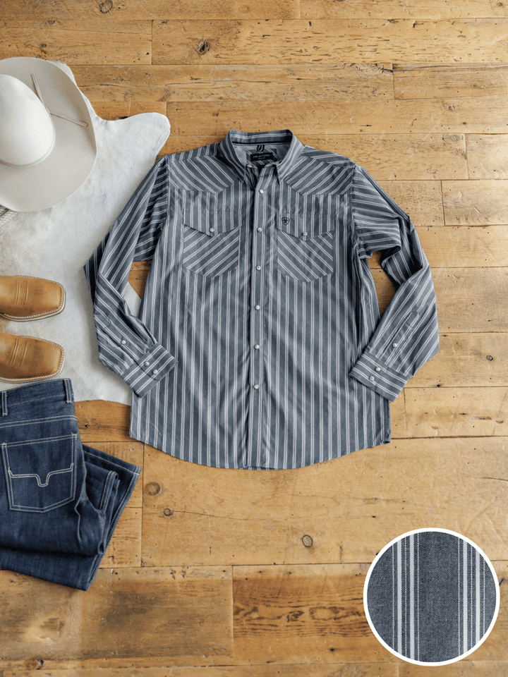 The Hallsville Ariat Men's Charcoal Pinstripe Button Up from Savannah Sevens western life{&}style is displayed on a wooden floor with blue jeans, brown boots, and a white cowboy hat. A close-up inset highlights the shirt's pinstripe fabric pattern.