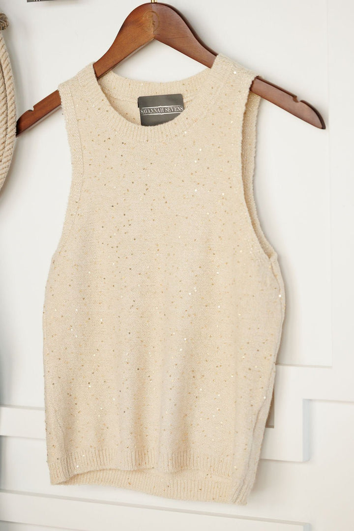 The Halsey Natural Woven Sleeveless Top by Savannah Sevens western life{&}style, featuring beige knit with subtle sparkle and gold sequins, hangs on a wooden hanger against a white background.