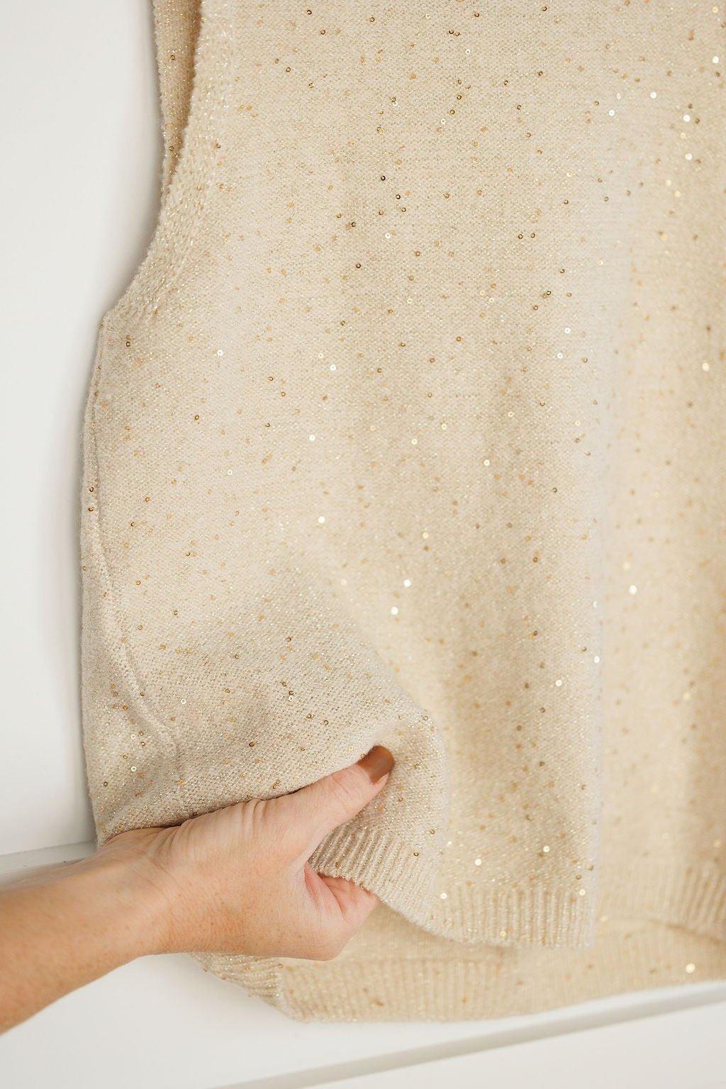 A hand holds the hem of the Savannah Sevens western life{&}style Halsey Natural Woven Sleeveless Top, emphasizing its subtly sparkly texture and scattered gold sequin details.