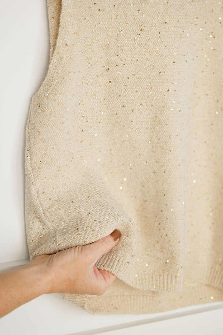A hand holds the hem of the Savannah Sevens western life{&}style Halsey Natural Woven Sleeveless Top, emphasizing its subtly sparkly texture and scattered gold sequin details.