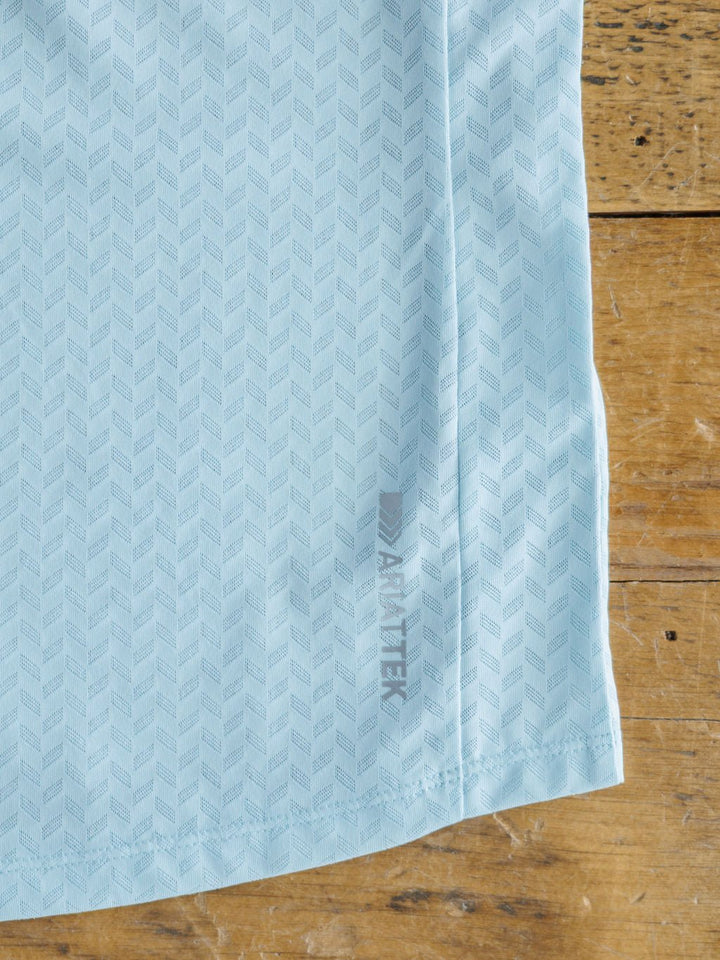 The Hanover Ariat Blue Golf Tank by Savannah Sevens western life{&}style features pastel blue mesh with a subtle geometric herringbone pattern, a small gray AEROREADY logo, and advanced cooling technology, displayed on rustic wood.