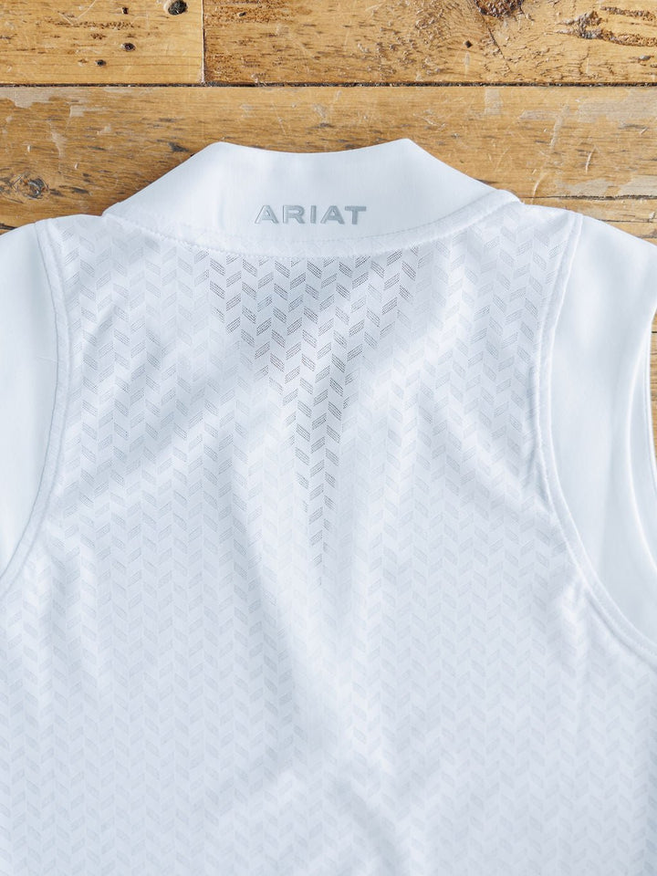 The Hanover Ariat White Golf Tank by Savannah Sevens western life{&}style features a subtle chevron pattern and "ARIAT" on the back collar, crafted from breathable mesh fabric and displayed on a rustic wooden surface.