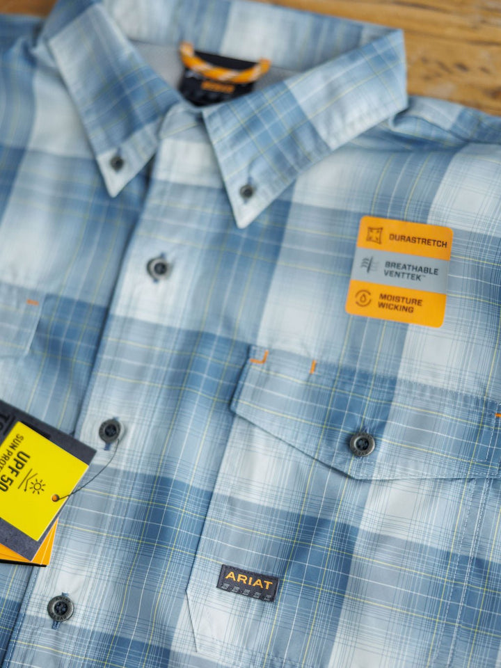 Close-up of the Harrison Ariat Men's Blue Plaid Button Up by Savannah Sevens western life{&}style, featuring DuraStretch, breathability, ventilation, and moisture-wicking properties. Ideal for comfort and performance. Displayed on a wooden surface.