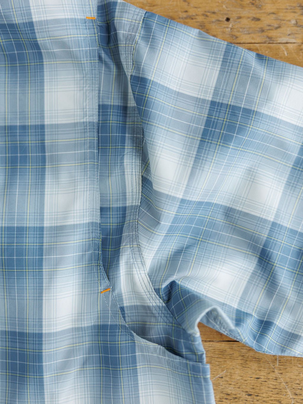 A close-up of the Harrison Ariat Men's Blue Plaid Button Up by Savannah Sevens western life{&}style, turned inside out to display underarm stitching and seams, is laid on a wooden surface—moisture-wicking and stylish.